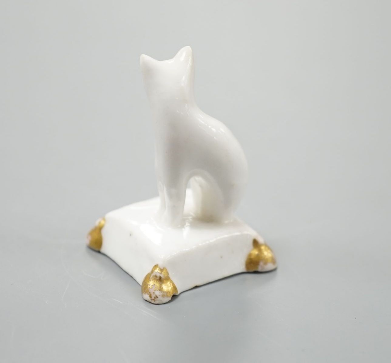 A rare English porcelain model of a cat seated on a cushion base, possibly Derby, c.1820-30, 4cm high, Provenance: Dennis G.Rice collection
